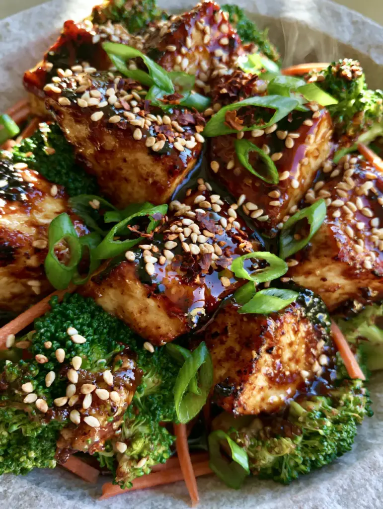 Close up of julienned carrots and seared chicken with toasted sesame seeds and scallion garnishes.