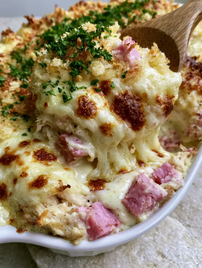 Side view of shredded chicken and ham layers in a creamy Dijon sauce within a white ceramic dish. (Chicken Cordon Bleu recipe)