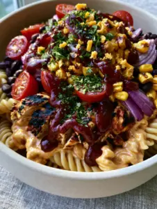 Close-up of al dente fusilli pasta coated in pale-orange ranch dressing with grilled chicken and roasted corn. (BBQ Chicken Pasta Salad)
