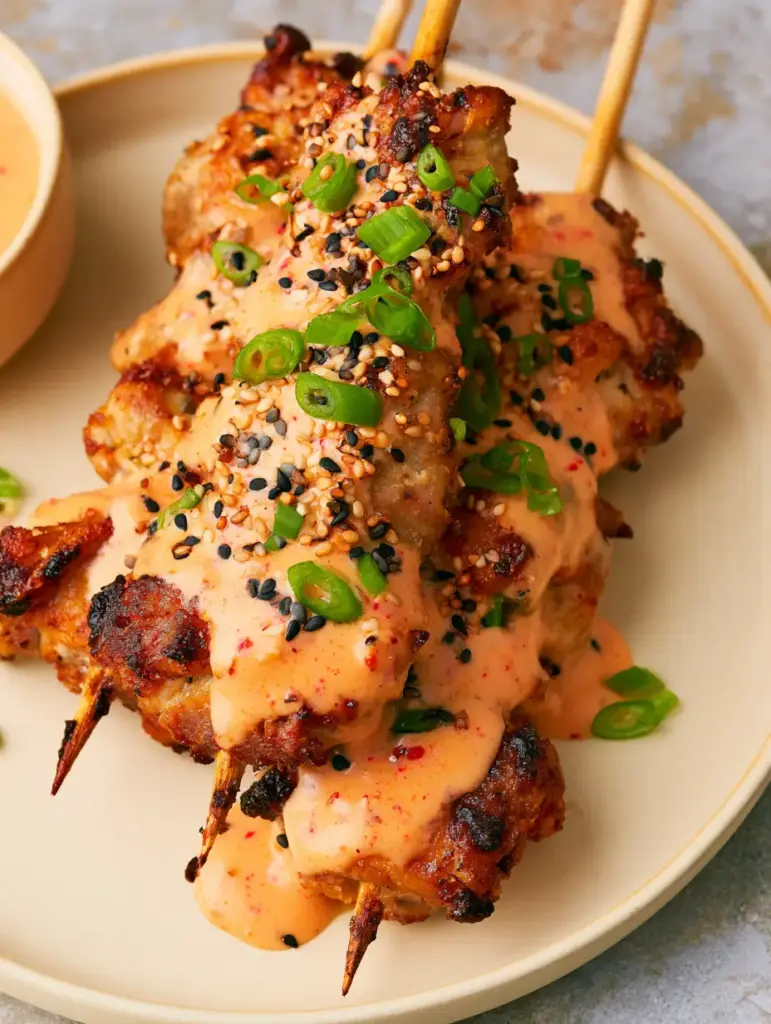 Air Fryer Bang Bang Chicken Skewers: Crispy, Charred, and Drizzled to Perfection 1 Detailed close-up of bite-sized air-fried chicken thighs on wooden skewers featuring toasted black and white sesame seeds and scallions.