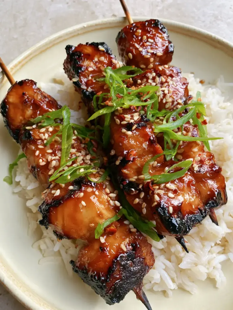 Detailed view of glossy chicken skewers resting on fluffy jasmine rice with visible toasted sesame seeds.