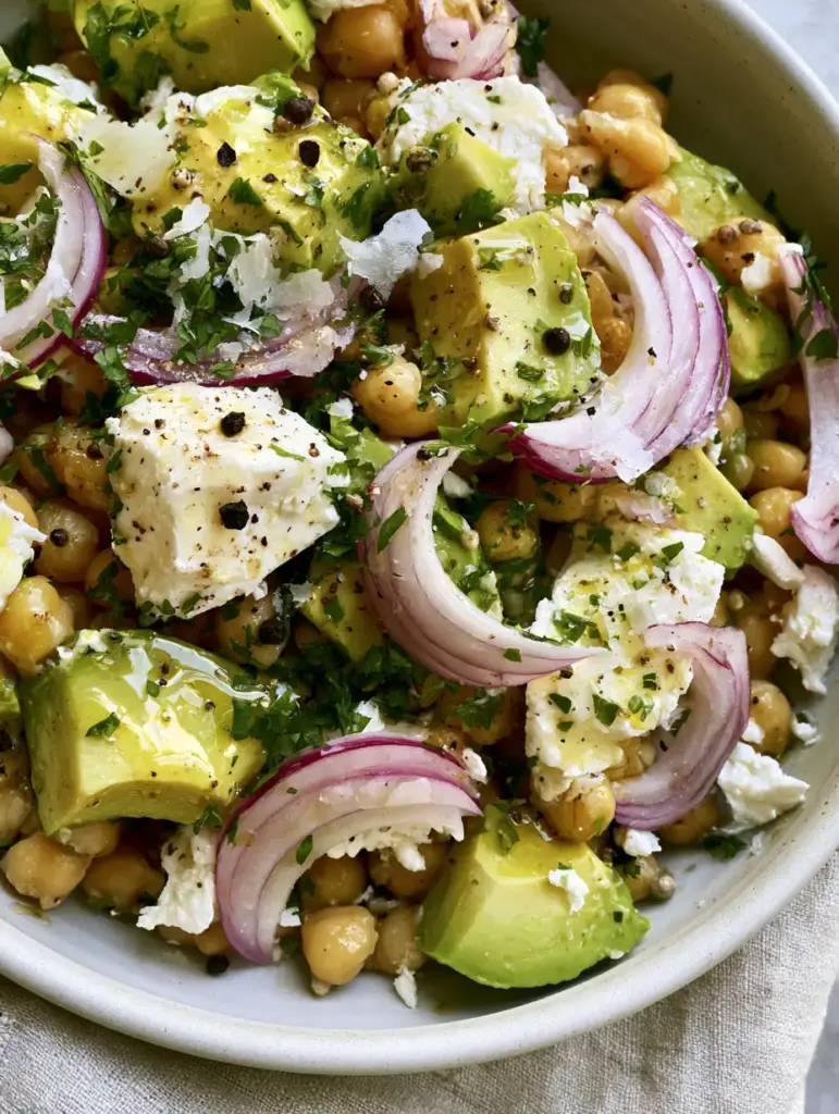 Rustic white feta crumbles and bright green parsley garnishing a Chickpea Feta Avocado Salad.