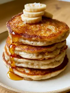 Extreme close up of a tall steaming stack of banana pancakes with lacy edges and maple syrup. (banana pancakes recipe)