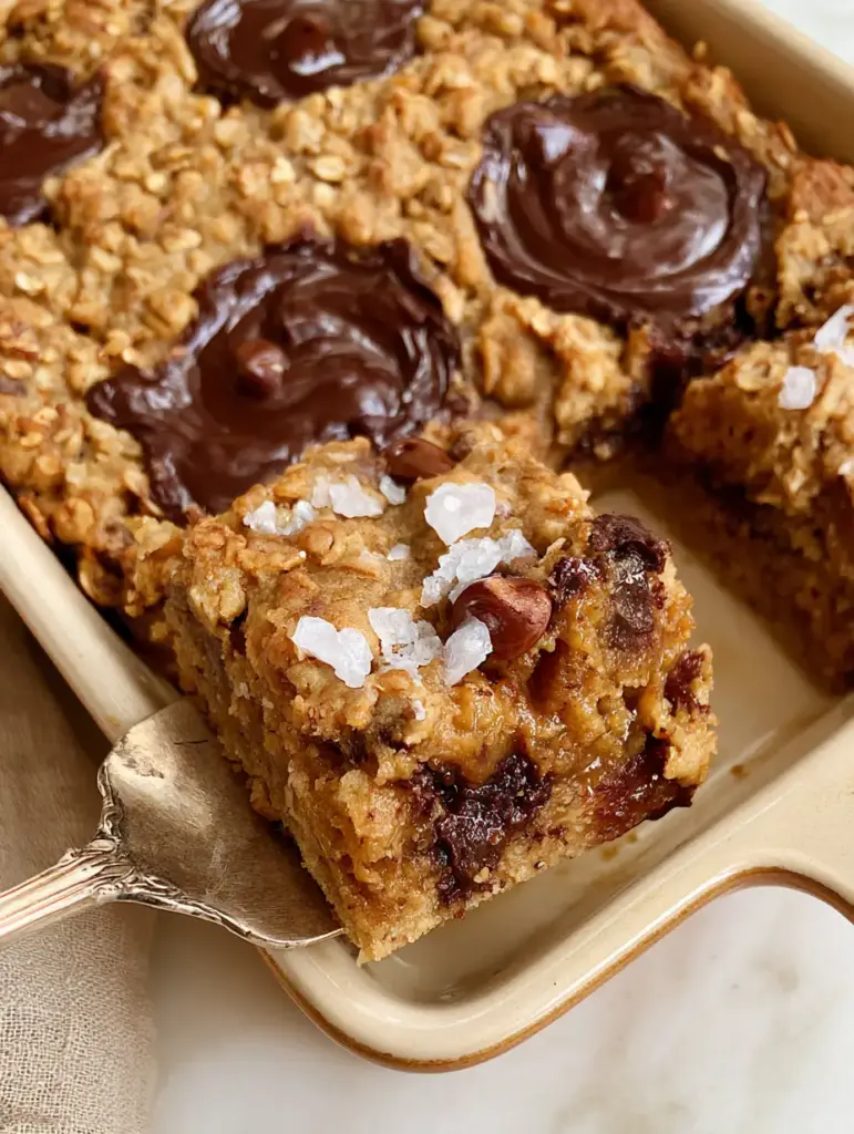 A silver server lifting a thick oatmeal cookie bar showing the soft, chewy interior and dark chocolate pockets.