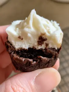 Extreme close-up of a single cheesecake brownie bite showing crinkled edges and glossy cheesecake peaks. (cheesecake brownie bites)