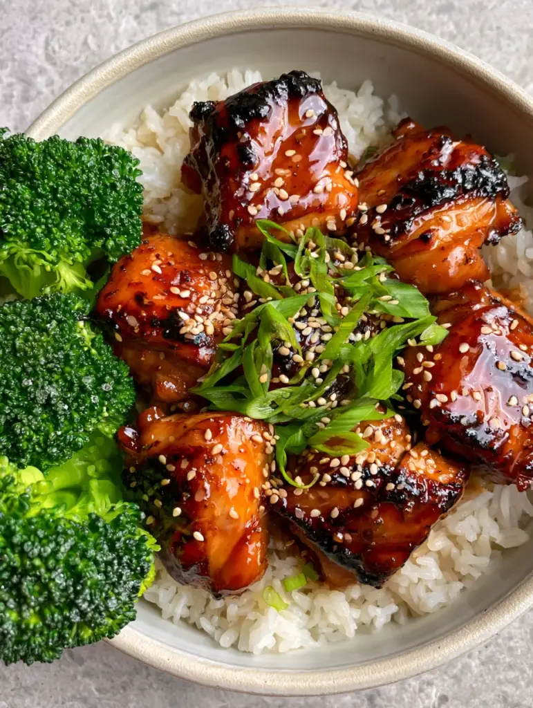 Teriyaki chicken served with fluffy jasmine rice and vibrant emerald broccoli florets showing water droplets.